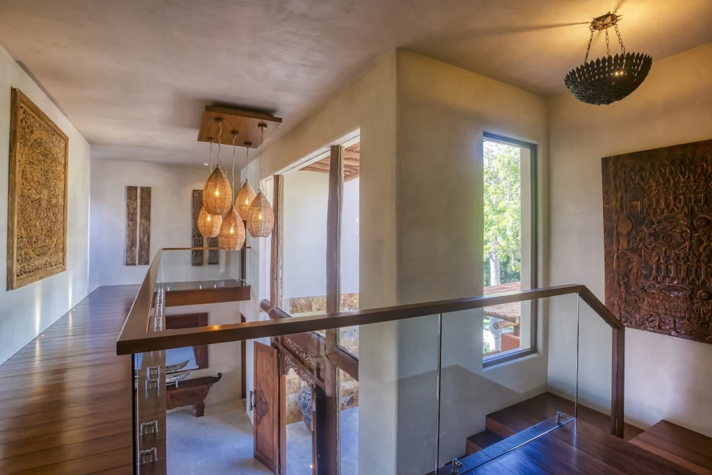 Open staircase gallery at Casa Dewi with glass railings, woven pendants and carved art