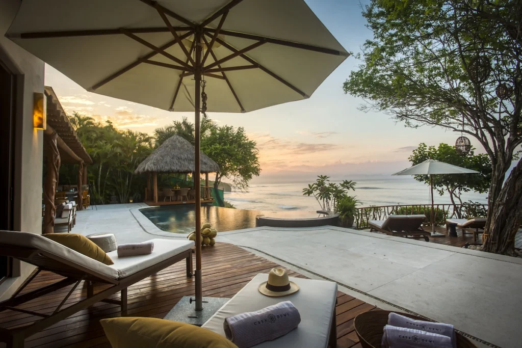 Casa Dewi infinity pool and ocean terrace at sunset with loungers and a palapa dining pavilion