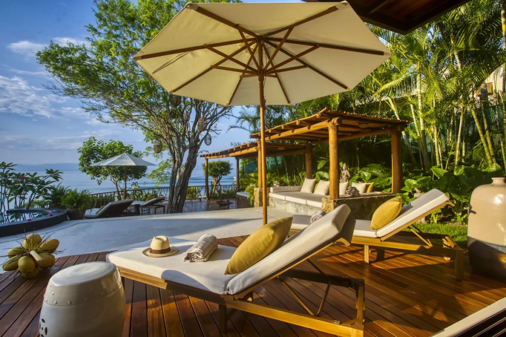 Sun loungers beside the Casa Dewi pool with tropical gardens and the Pacific beyond