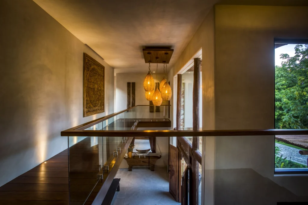 Upper gallery at Casa Dewi at dusk with woven pendant lights and glass railings