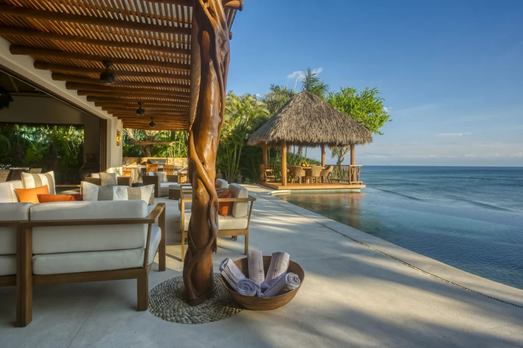 Shaded lounge terrace beside Casa Dewi's infinity pool with a palapa dining pavilion over the Pacific