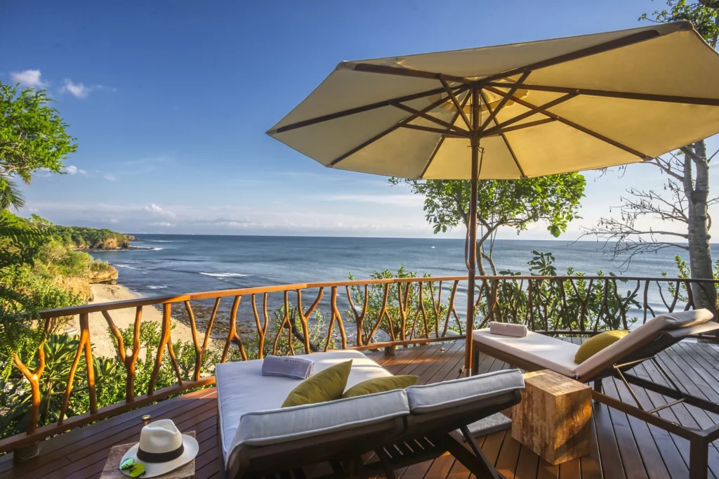Ocean-view sun deck at Casa Dewi with loungers and an umbrella above a sandy cove