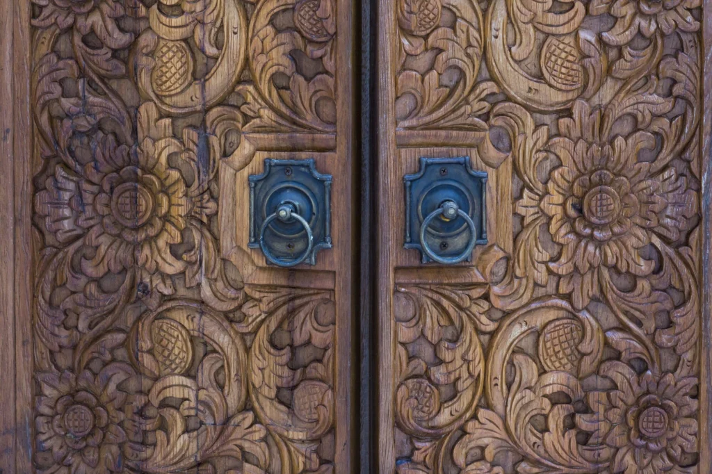 Close view of floral carvings and metal ring handles on Casa Dewi's wooden doors