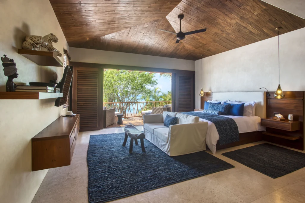 King bedroom at Casa Dewi with blue textiles, a sitting area and an ocean-view balcony