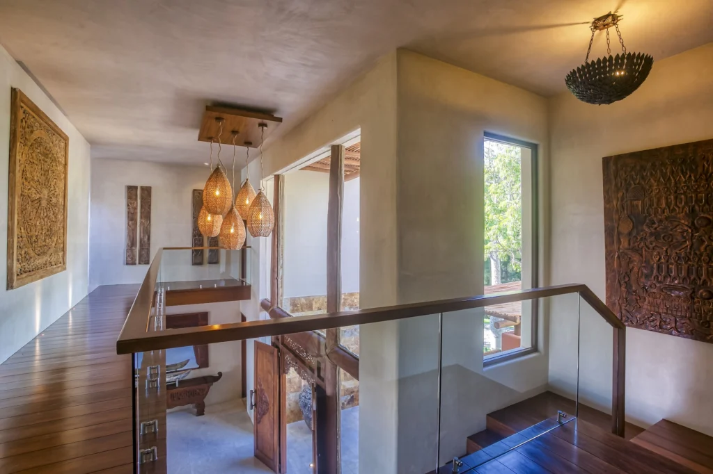 Upper landing at Casa Dewi with woven pendant lights, glass railings and carved wall panels