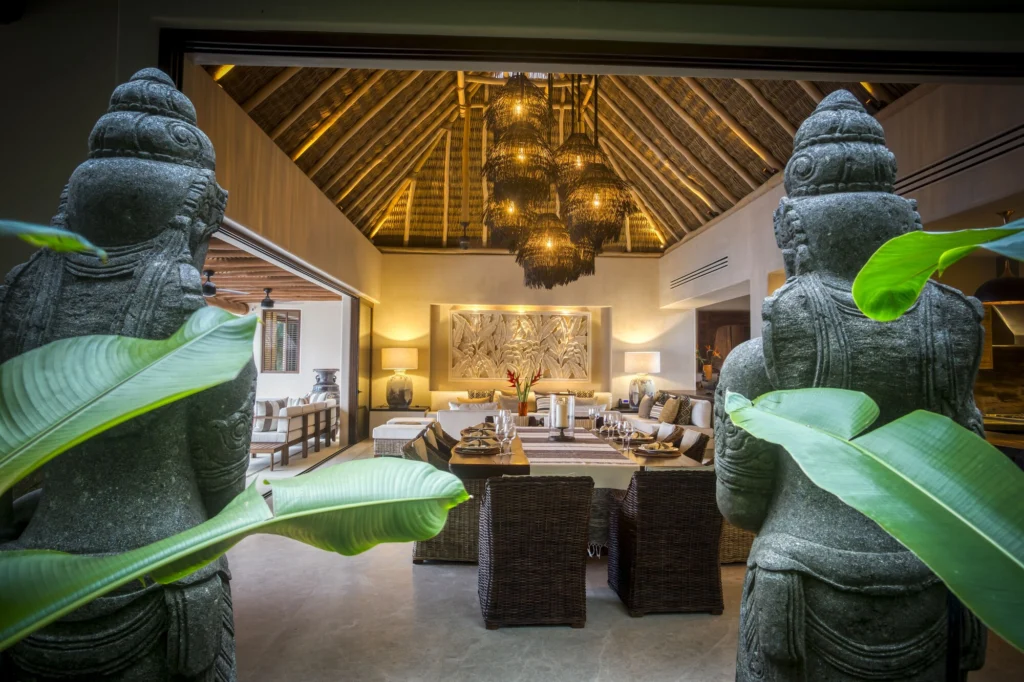 Casa Dewi dining room viewed between stone sculptures and tropical leaves