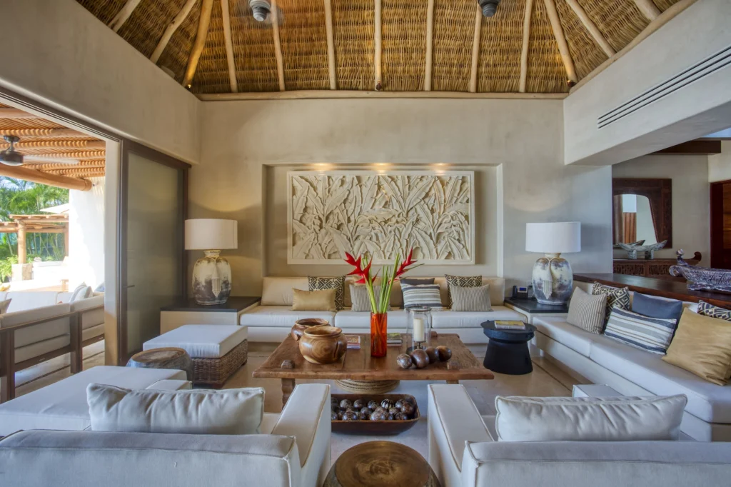 Palapa-roofed living room at Casa Dewi with white sofas, carved tropical art and garden views