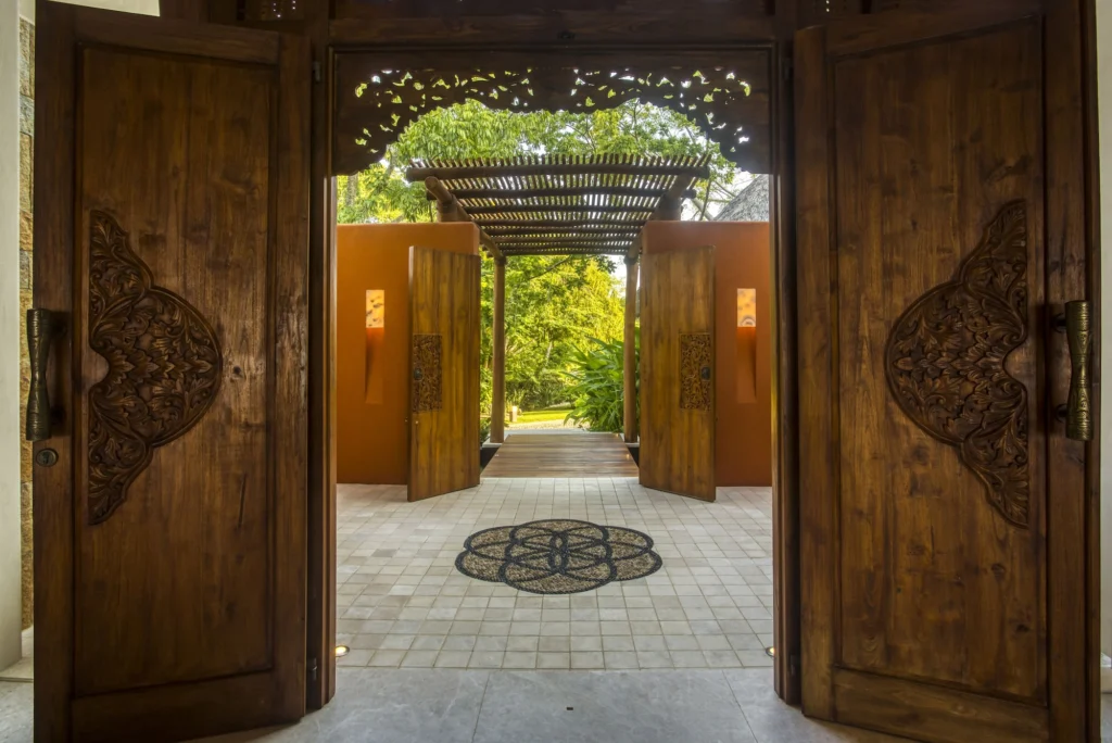 View through Casa Dewi's carved wooden doors toward the tropical garden entrance