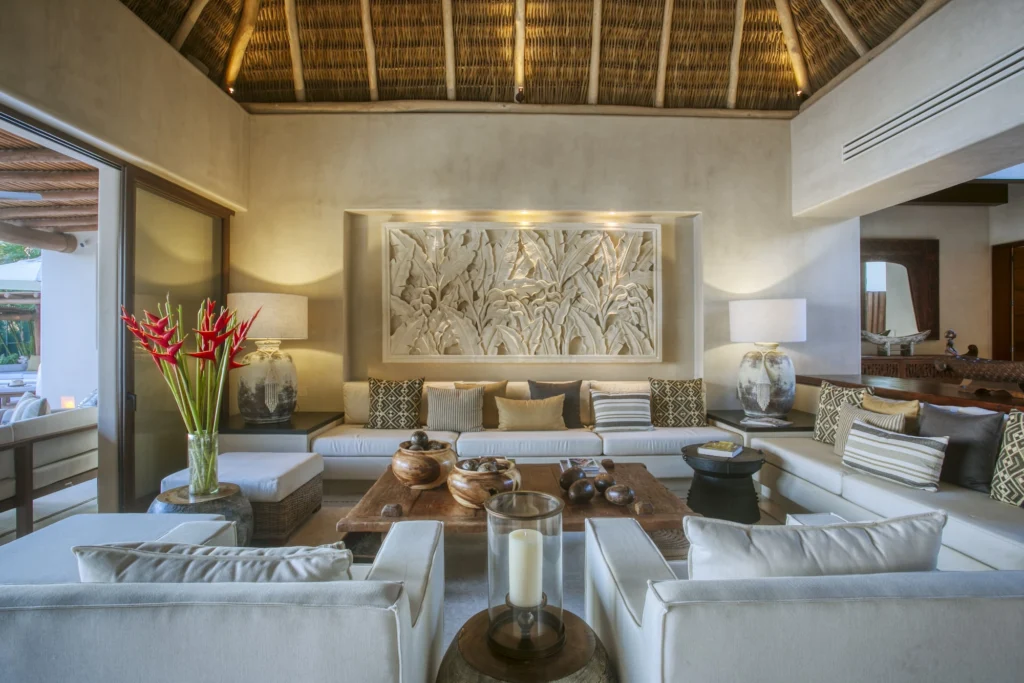 Casa Dewi living room with white sofas beneath a palapa roof and illuminated carved artwork