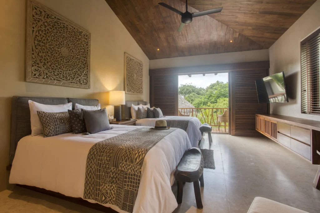 Guest bedroom at Casa Dewi with two beds, carved panels and doors opening to a balcony